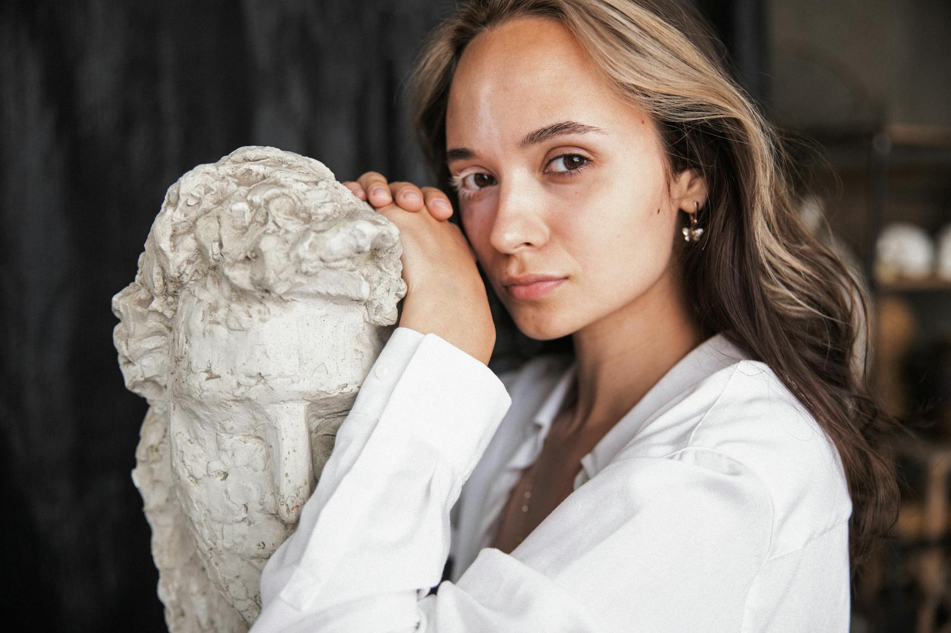 woman in white top looking at the camera while leaning on a sculpture